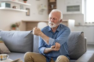 Person sits on sofa at home holding elbow with painful facial expression