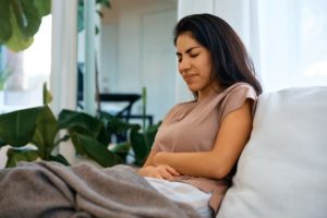 Woman sitting on sofa holding abdomen in pain