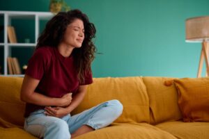 Person suffering from abdominal pain while sitting on sofa in living room